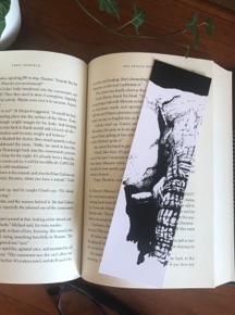 An ink drawing of an elephant on a bookmark sitting on a page of a book. 